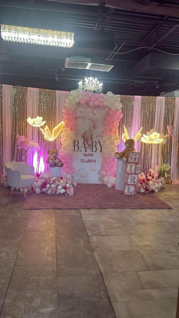 Pink and gold baby shower backdrop with balloon arch in the banquet hall